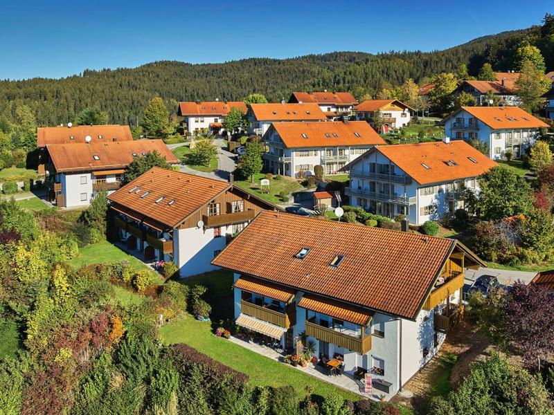 Haus mit roten Dächern in einer grünen Hügellandschaft unter blauem Himmel.