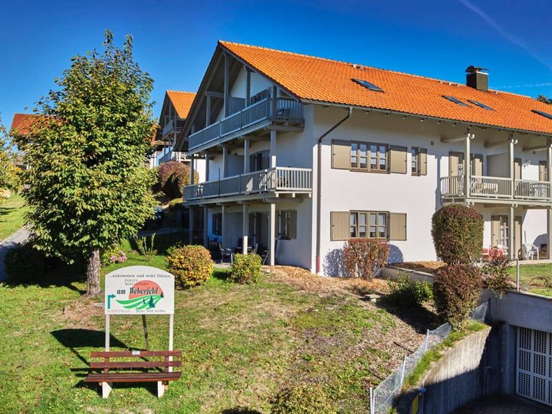 Großes Ferienhaus mit braunem Dach, Balkon und grünem Garten bei sonnigem Wetter.