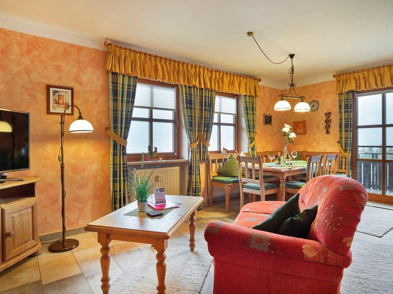 Gemütliches Wohnzimmer mit rotem Sofa, Holztisch und Essbereich mit großem Fenster.