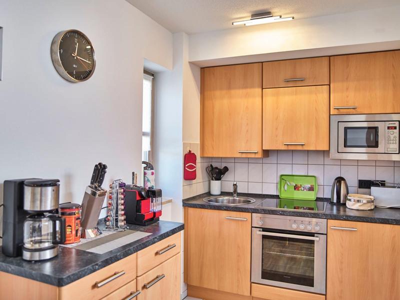 Moderne Küchenecke mit hellen Holzschränken, Kaffeemaschine und Mikrowelle.