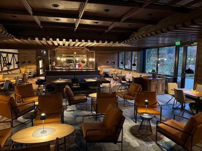 Acogedor bar de hotel con sillones de cuero, mesas de madera y techo con vigas de madera.