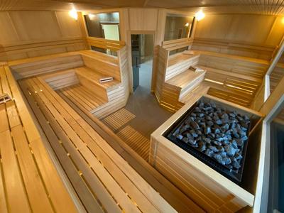 Wnętrze nowoczesnej, jasnej sauny z drewnianymi ławkami i piecem na kamienie.