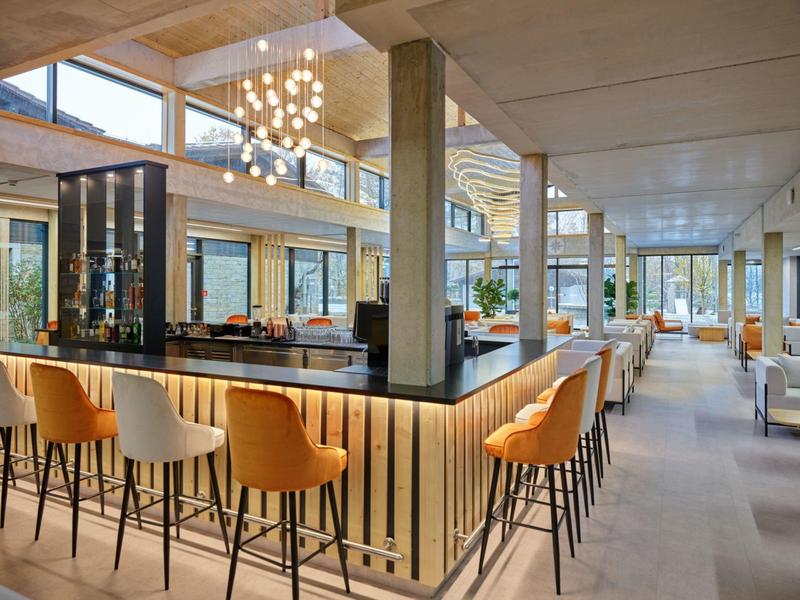 Elegancki bar hotelowy z pomarańczowymi hokerami i nowoczesnym designem.