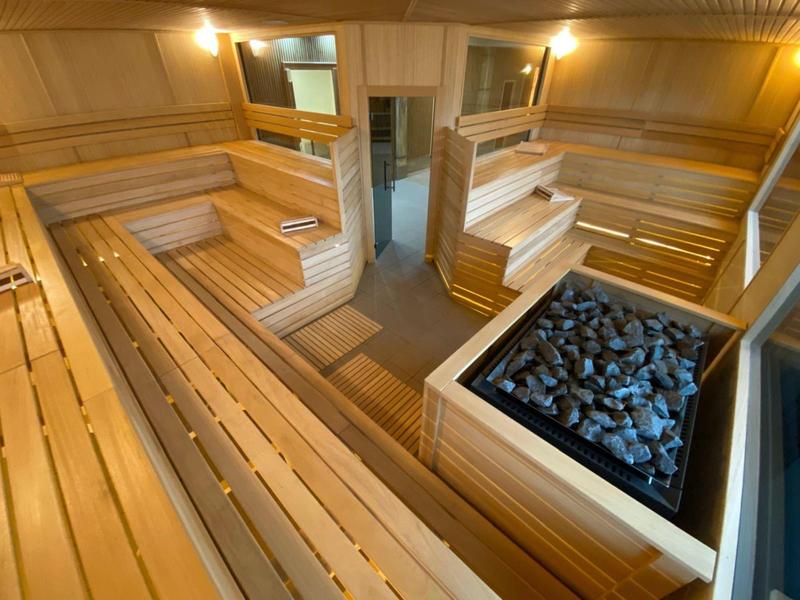 Wnętrze nowoczesnej, jasnej sauny z drewnianymi ławkami i piecem na kamienie.
