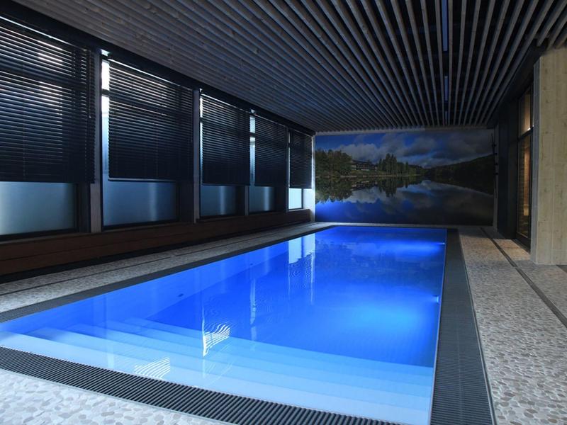 Basen kryty z niebiesko oświetloną wodą i dużym zdjęciem krajobrazu na ścianie.