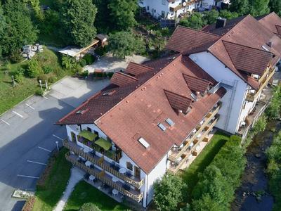 Groot hotelgebouw met rode daken, omgeven door groen en een parkeerplaats aan de linkerkant.