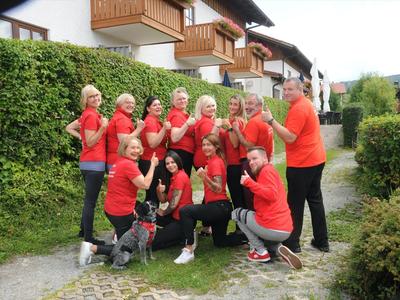 Gruppo di persone con magliette rosse che posano sorridendo in un cortile con siepi verdi.