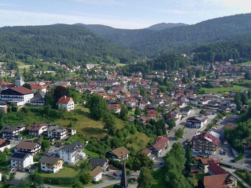 Widok na małe miasteczko z wieloma domami, otoczone zielonymi wzgórzami i górami w tle.