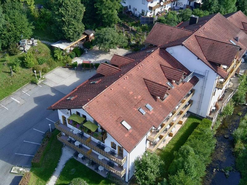 Duży budynek hotelowy z czerwonymi dachami, otoczony zielenią i parkingiem po lewej stronie.
