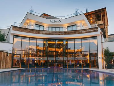 Modernes Hotelgebäude mit großen Glasfenstern und beleuchtetem Außenpool bei Dämmerung