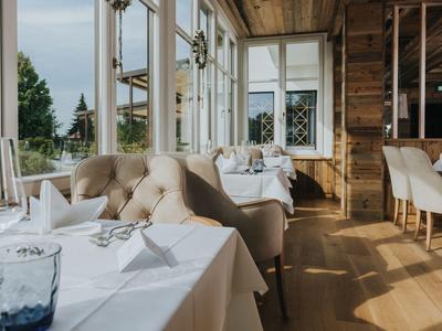 Restaurant lumineux avec grandes fenêtres, tables blanches et fauteuils beige confortables.