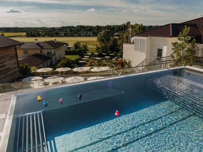 Ein klarer Pool mit bunten Ballspielzeugen auf einer Terrasse mit Blick auf grüne Felder und Gebäude.
