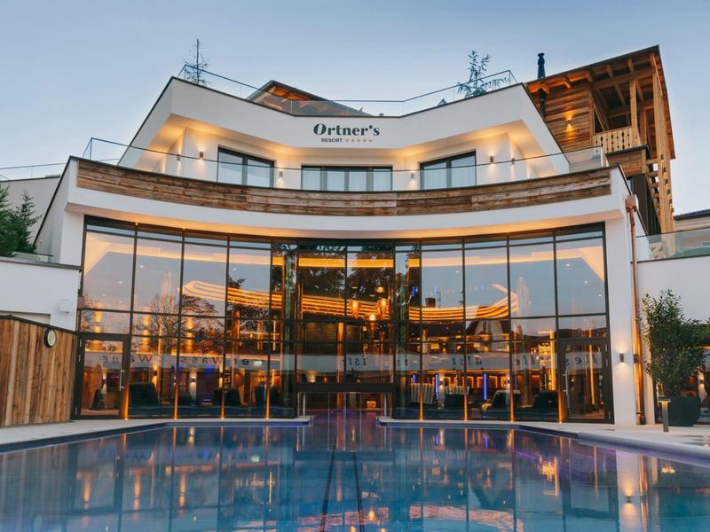 Modernes Hotelgebäude mit großen Glasfenstern und beleuchtetem Außenpool bei Dämmerung