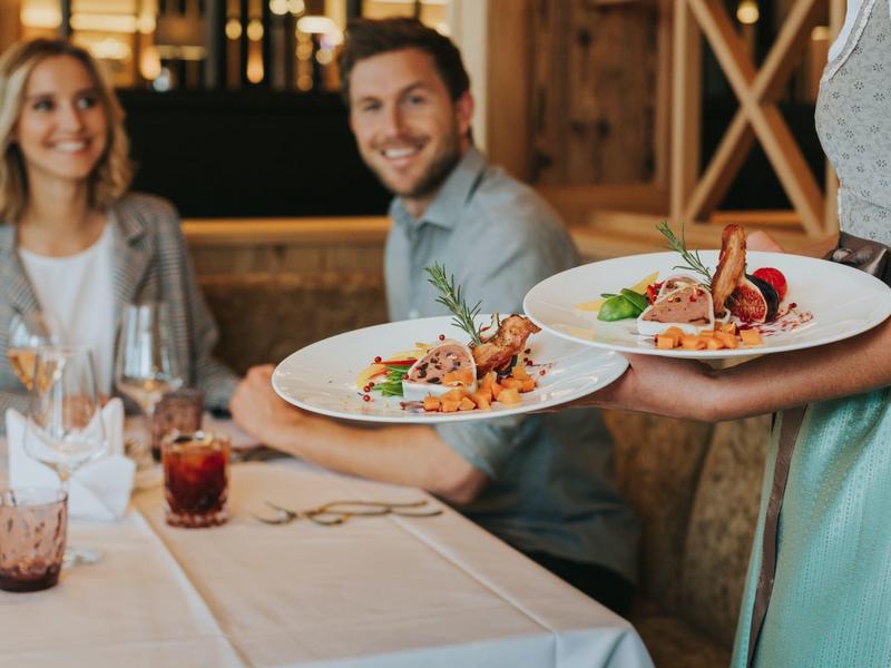 Zwei Teller mit appetitlichem Essen werden in einem Restaurant serviert, Gäste im Hintergrund.