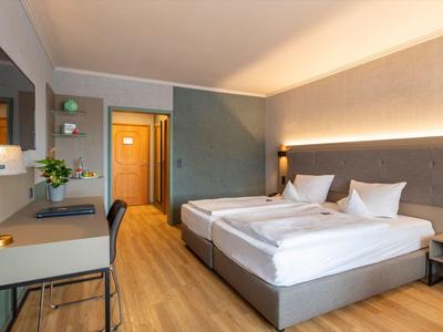 Modernes Hotelzimmer mit zwei Einzelbetten, Schreibtisch und Holzfußboden.