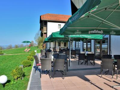 Terrasse mit schwarzem Mobiliar und Sonnenschirmen neben einem weißen Gebäude mit Blick auf grüne Wiesen.