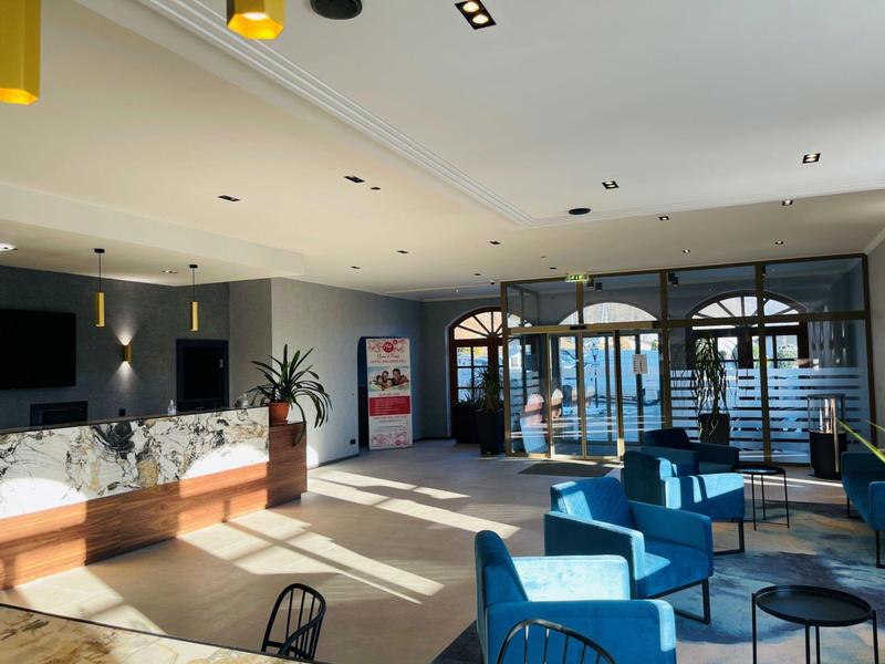 Jasna recepcja hotelowa z niebieskimi meblami, marmurowym kontuarem i dużym oknem z widokiem na zewnątrz.