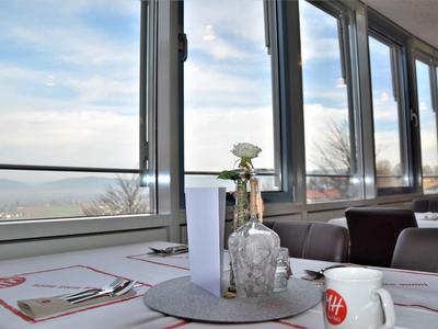 Tisch mit Dekoration und Tasse in einem Raum mit großen Fenstern und Blick auf den Himmel.