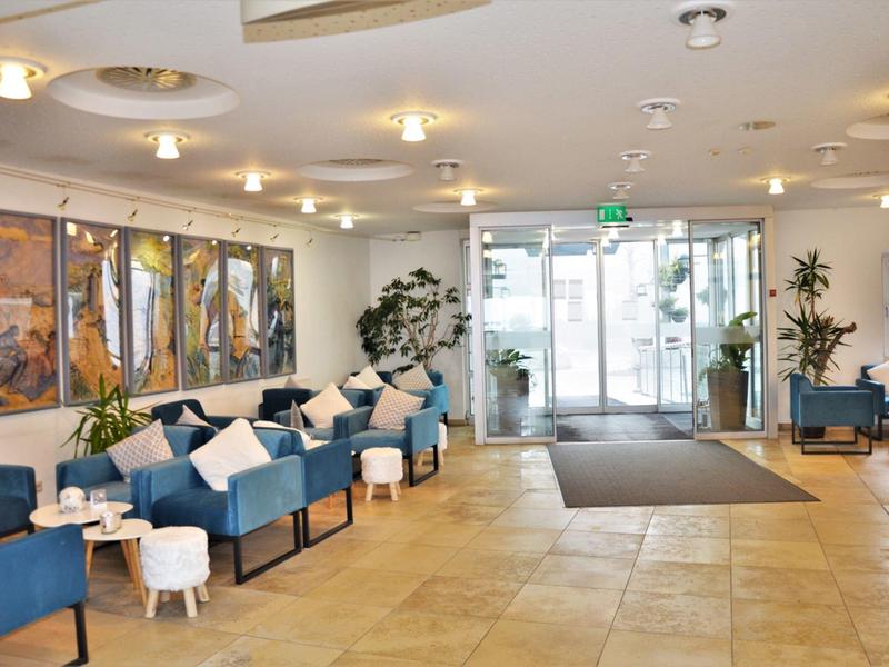 Heller Hotel-Lobby mit blauen Sesseln, Kissen und modernen Kunstwerken an den Wänden.