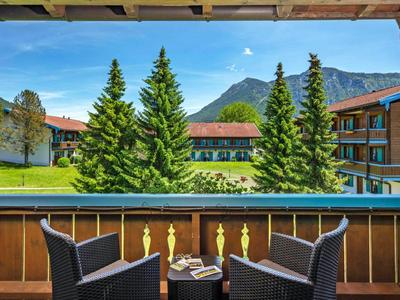 Balcón con dos sillas, mesa pequeña y vista a abetos y montañas al fondo.