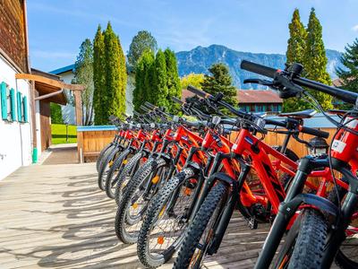Varias bicicletas rojas están alineadas en una terraza de madera frente a un edificio en las montañas.