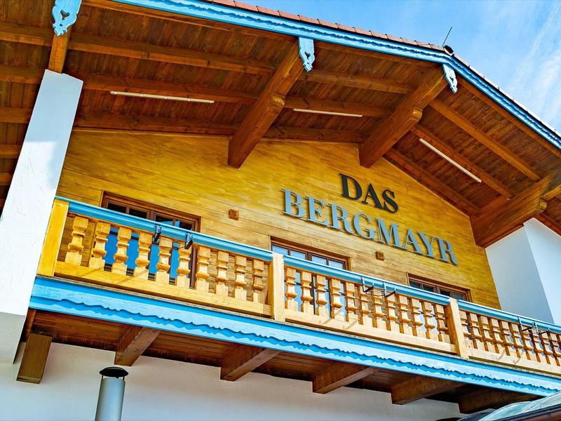 Balcony of a traditional mountain hotel with wooden beams and sign reading Das Berglair.