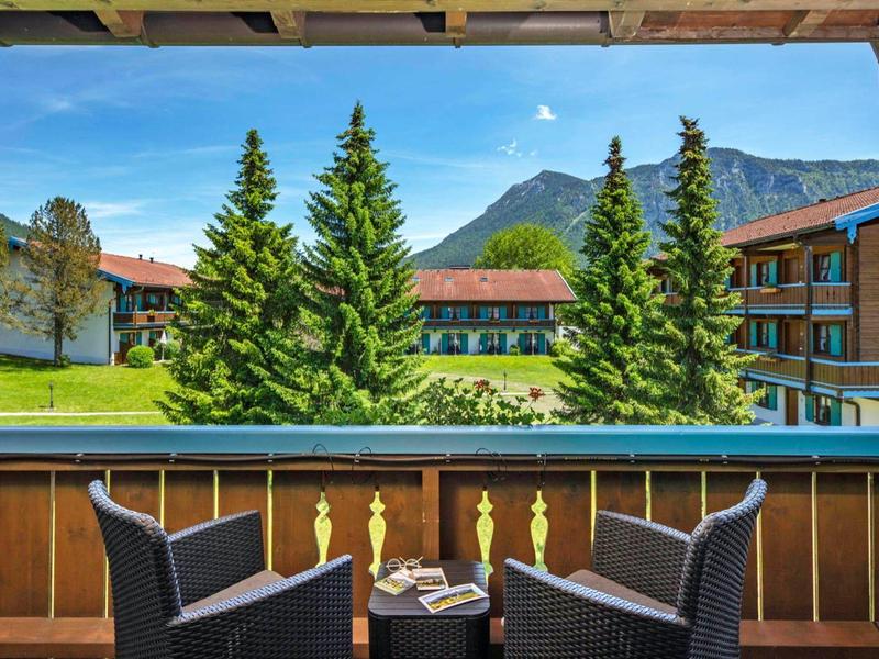 Balcony with two chairs overlooking green fir trees and a hotel building in front of mountains.