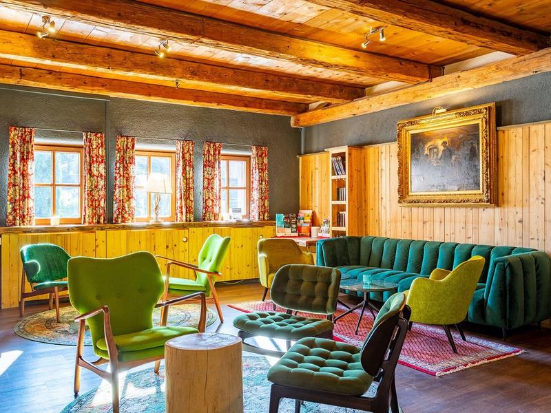 Bright living room with wooden beams, green armchairs, sofa, and colorful curtains on windows.