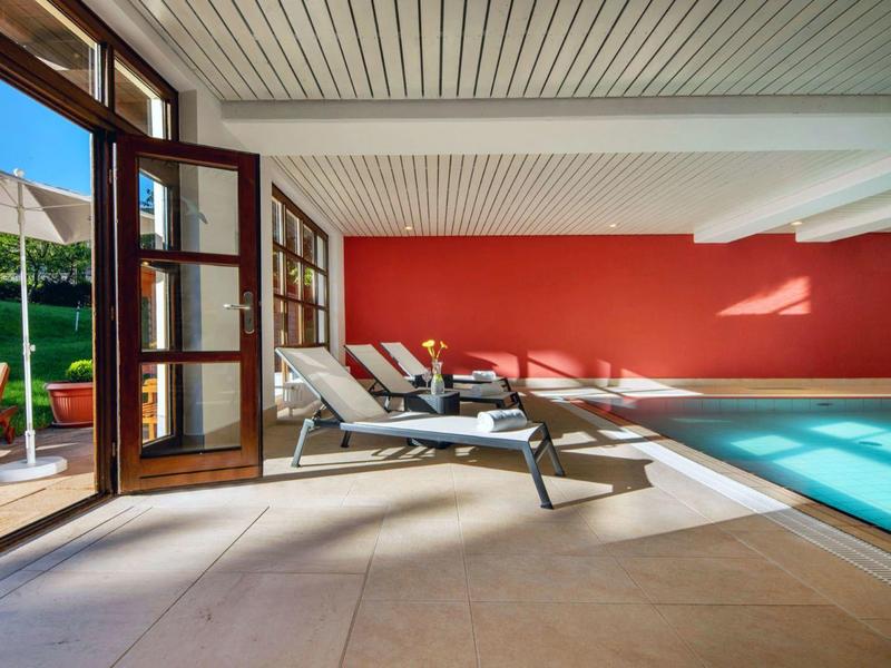 Modern indoor pool with lounge chairs and view outside through open glass doors.