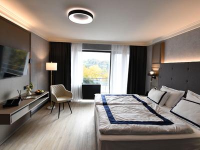 Modernes Hotelzimmer mit Doppelbett, Sessel, Wandfernseher und Balkon mit Ausblick.