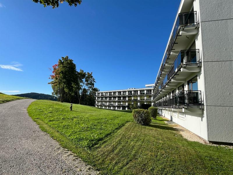Edificio moderno de hotel con balcones, rodeado de césped verde y cielo azul despejado.