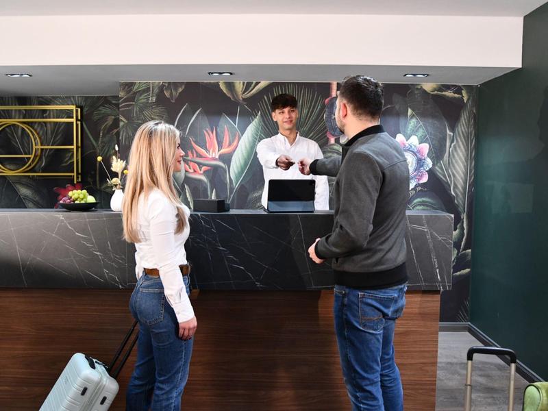 Recepcionista de hotel atendiendo a dos huéspedes en un mostrador con decoración moderna.