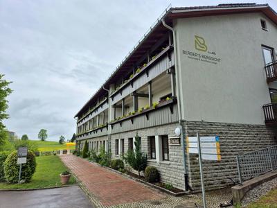 Außenansicht eines mehrstöckigen Hotels mit Balkon und angrenzendem Grünbereich bei bewölktem Himmel.