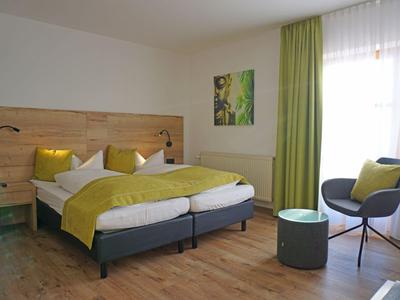 Modernes Hotelzimmer mit Doppelbett, grünen Vorhängen und Sitzbereich mit Stuhl und Tisch.