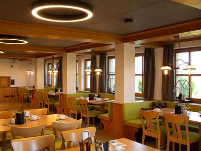 Gemütlicher Speisesaal mit Holzmöbeln, großen Fenstern und modernen Deckenleuchten.