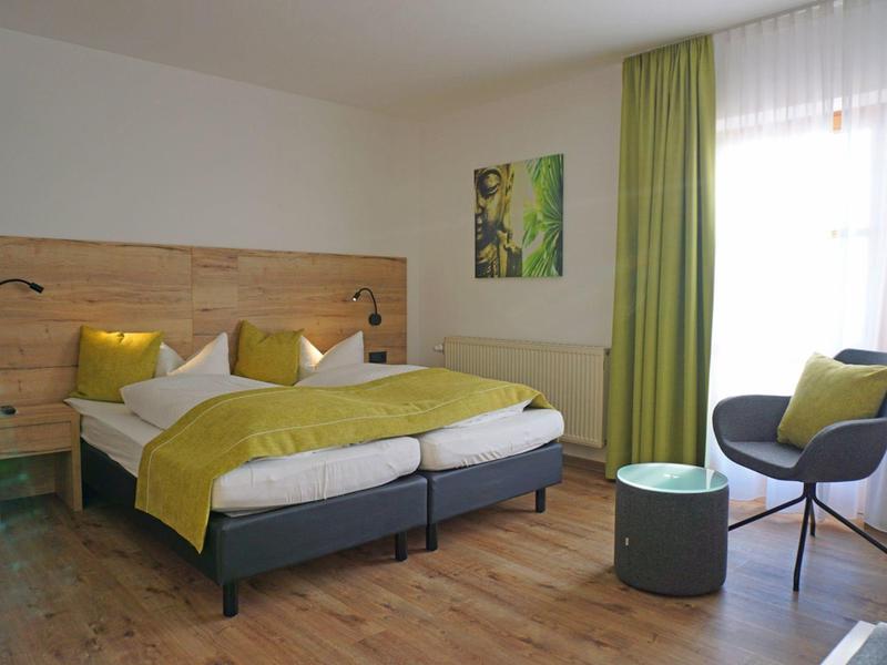 Modernes Hotelzimmer mit Doppelbett, grünem Vorhang und Stil mit Stuhl und kleinem Tisch.