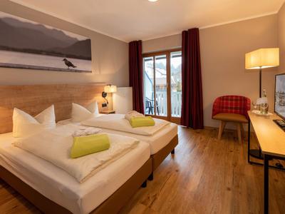 Příjemný hotelový pokoj s manželskou postelí, dřevěnou podlahou, psacím stolem a balkonem s výhledem ven.