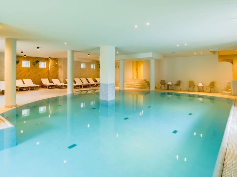Vnitřní bazén s lehátky a světlým interiérem v hotelu