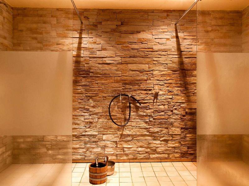Sprcha s dešťovou hlavicí a dřevěným kýblem v elegantním interiéru s kamennou zdí.