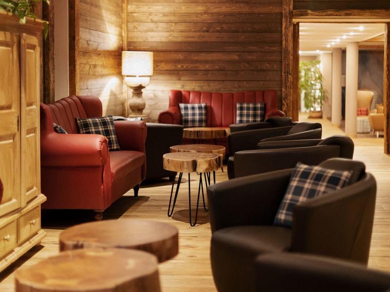 Pohodlný hotelový salonek s koženými křesly, dřevěnými stolky a teplým dřevěným dekorem.