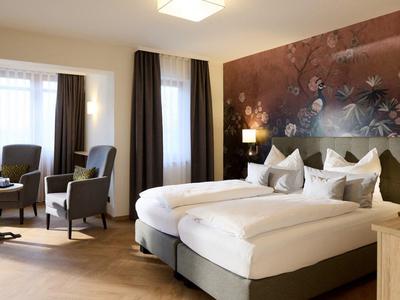 Pokój hotelowy z dwoma pojedynczymi łóżkami, częścią wypoczynkową z krzesłami i dużym muralem na ścianie.