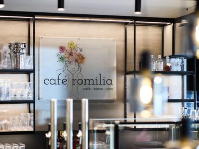Area caffè moderna con scaffali in vetro e insegna illuminata 'Cafe Romilia'.