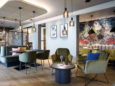 Area salotto moderna in hotel con tavoli, poltrone e lampade a sospensione.