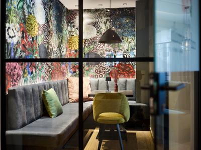 Angolo accogliente dell'hotel con divano, panca, sedia verde e decorazione murale colorata.