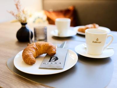 Stół śniadaniowy z rogalikiem, tabliczką czekolady i kawą na białej zastawie.