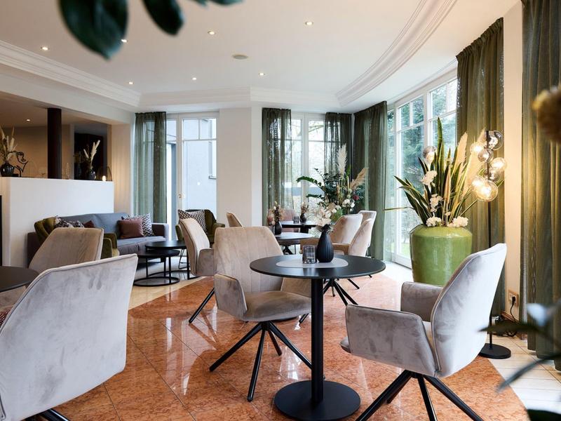 Stylowa przestrzeń lounge w hotelu z wygodnymi fotelami, stolikami i dużymi oknami.