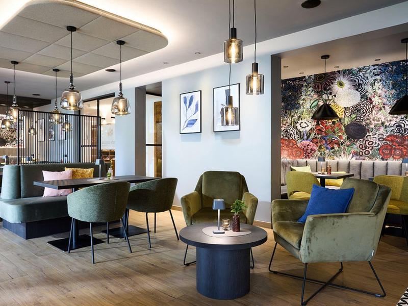 Nowocześnie urządzone lobby hotelowe z wygodnymi fotelami, stołami i dekoracyjną sztuką ścienną.