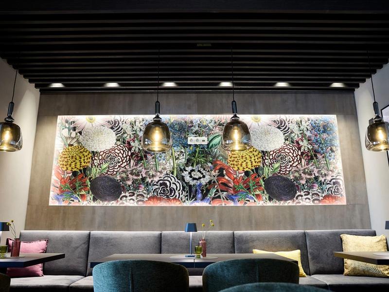 Nowoczesna przestrzeń lounge w hotelu z kolorową abstrakcyjną sztuką ścienną i wiszącymi lampami.