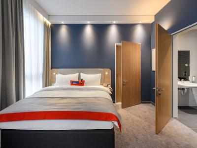 Modernes Hotelzimmer mit blau gestrichener Wand, großem Bett und angrenzendem Bad.
