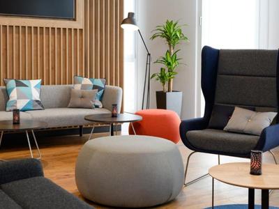 Modern eingerichteter Hotel-Loungebereich mit Sesseln, Sofas und Tischen in warmem Licht.